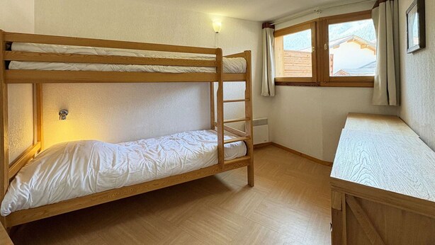 Ein Schlafzimmer mit Etagenbetten, Holzboden, einem Fenster mit Vorhängen und einer Wandleuchte.