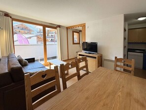 A cozy living room with a sofa, wooden chairs, a small table, and a television. - Ski-in/ski-out apartment - 8 guests (Les Orres)