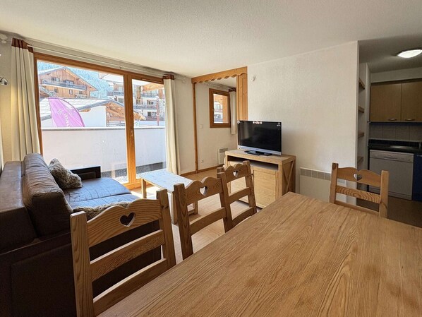 Kodikas olohuone, jossa on sohva, puutuoleja, pieni pöytä ja televisio.