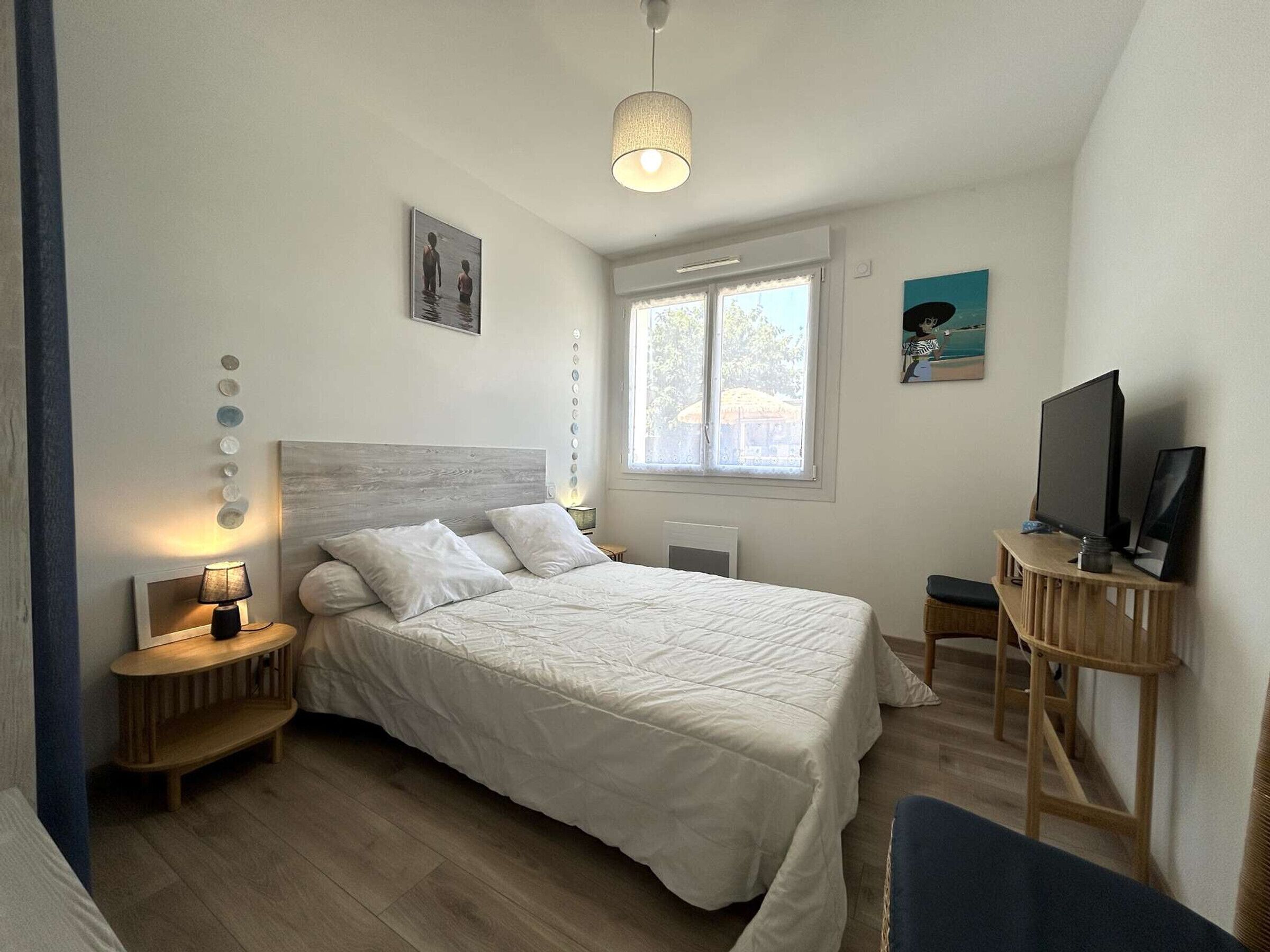 Un dormitorio con cama, mesitas de noche, televisor y ventana.