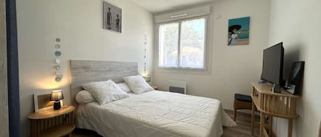 Un dormitorio con cama, mesitas de noche, televisor y ventana.