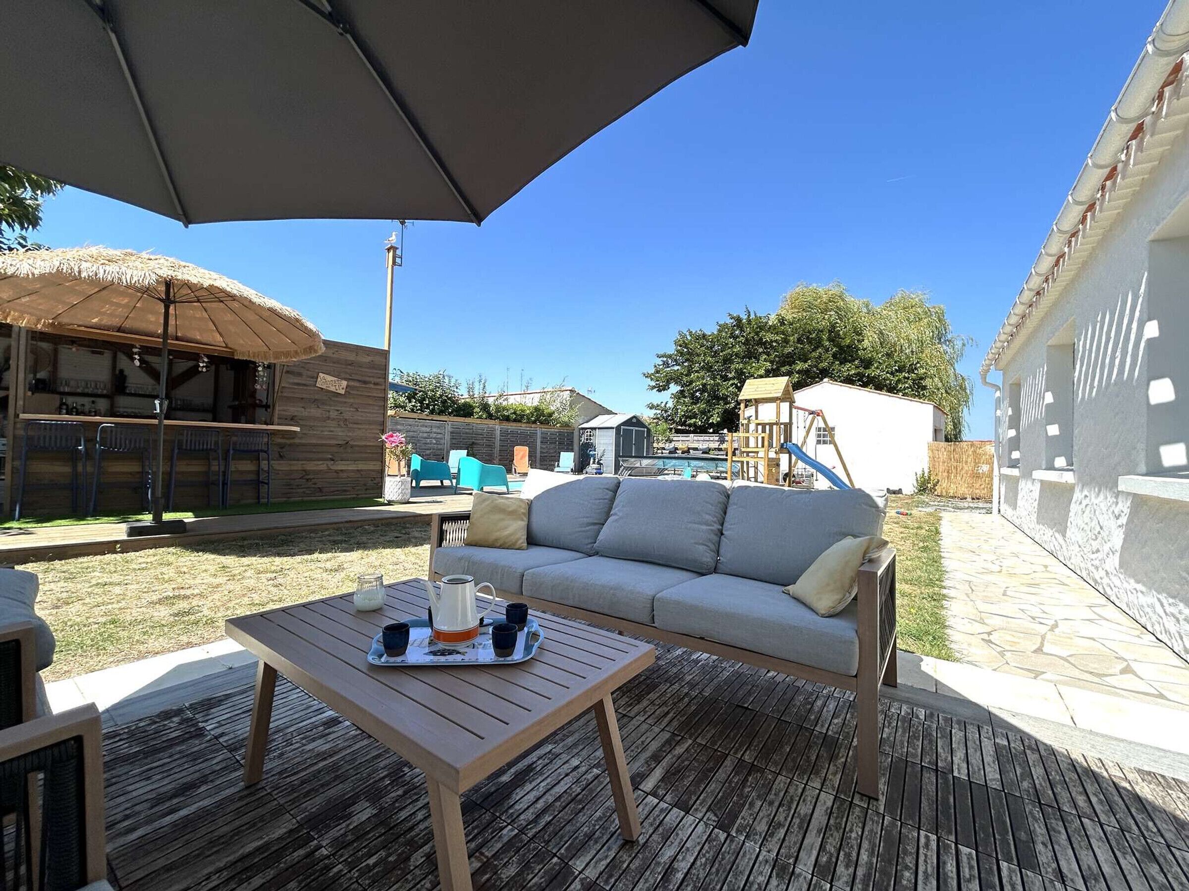 An outdoor patio with a wooden table, a grey sofa, and a large umbrella.