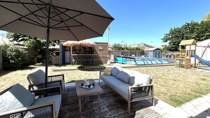 Eine Außenpatio mit Holzdeck, einer gepolsterten Couch, einem Tisch mit einem Krug und einem großen Sonnenschirm.
