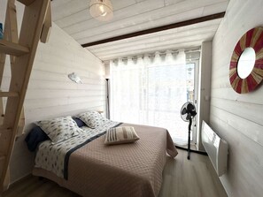Une chambre à coucher avec un lit, une échelle, une lampe sur pied et une fenêtre avec des rideaux.