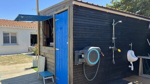 Ein kleines Freigelände mit einer blauen Tür, einer Toilette, einem Urinal und einer Dusche.