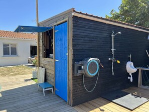 Ein kleines Freigelände mit einer blauen Tür, einer Toilette, einem Urinal und einer Dusche.