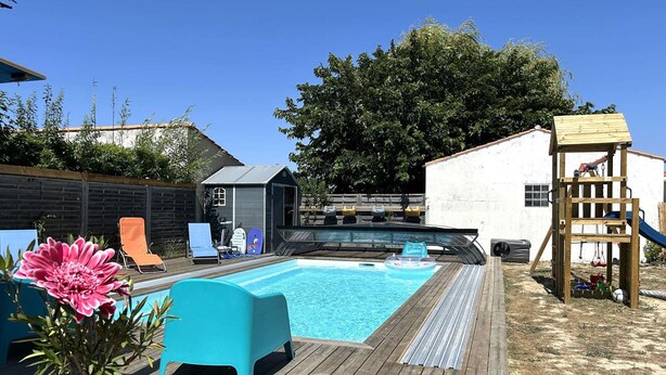 Ein Garten mit Schwimmbad, einer Holzterrasse, einer Spielanlage und einem kleinen Gartenhaus.