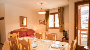 A dining area with a table set for two, a bed with red bedding, a television, and a window with curtains. - Comfortable apartment for 6 with terrace in Aussois (Aussois)
