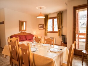 A dining area with a table set for two, a bed with red bedding, a television, and a window with curtains. - Comfortable apartment for 6 with terrace in Aussois (Aussois)