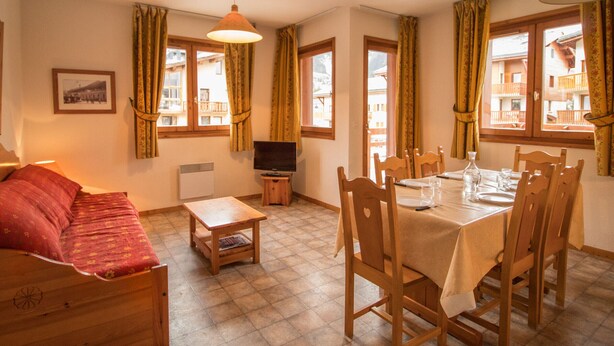 A room with a bed, a TV, a dining table set for four, and a window with curtains. - Comfortable apartment for 6 with terrace in Aussois (Aussois)