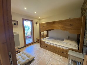 Une chambre avec un lit superposé en bois, une petite table de chevet, une chaise et une vue sur un balcon.