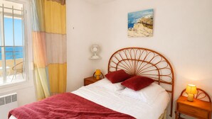 A bedroom with a bed, a nightstand, a wall-mounted fan, a window with curtains, and a painting. - Air-conditioned apartment, sea view - 4/6 guests (Sète)