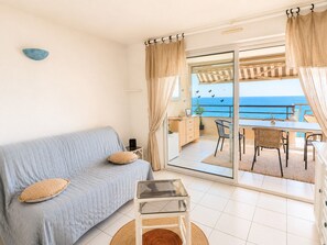 Ein Zimmer mit einer Couch, einem kleinen Tisch und Meerblick durch eine Glastür.