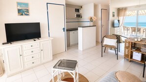 A modern living room with a flat-screen TV, a dining area with wicker furniture, and a kitchen with white cabinets and a microwave. - Air-conditioned apartment, sea view - 4/6 guests (Sète)
