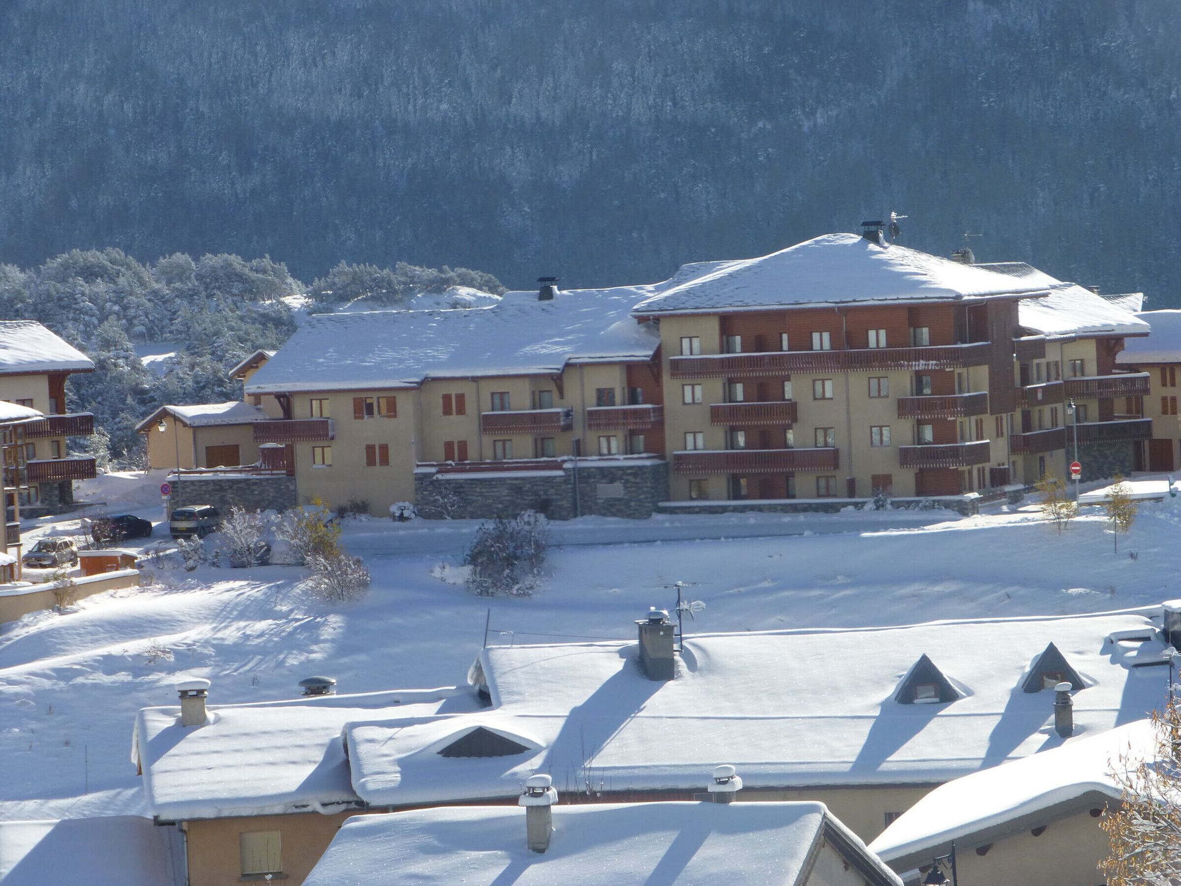Un hotel de varios pisos con balcones, un paisaje nevado y montañas al fondo.
