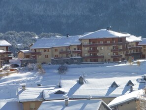 A multi-story hotel with balconies, a snow-covered landscape, and a mountainous backdrop. - Comfortable apartment - 4 guests (Aussois)