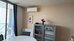 A modern room with a marble table, a grey cabinet with glass doors, a mounted air conditioner, and a window with a view. - Stunning T2 AC, sea view - 4 guests (Sète)