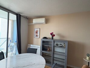 Quarto moderno com mesa de mármore, um armário cinza com portas de vidro, ar condicionado fixado na parede e janela com vista.