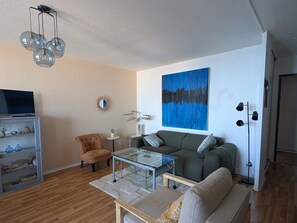 Ein Wohnzimmer mit Sofa, Sessel, Glastisch und Fernseher.