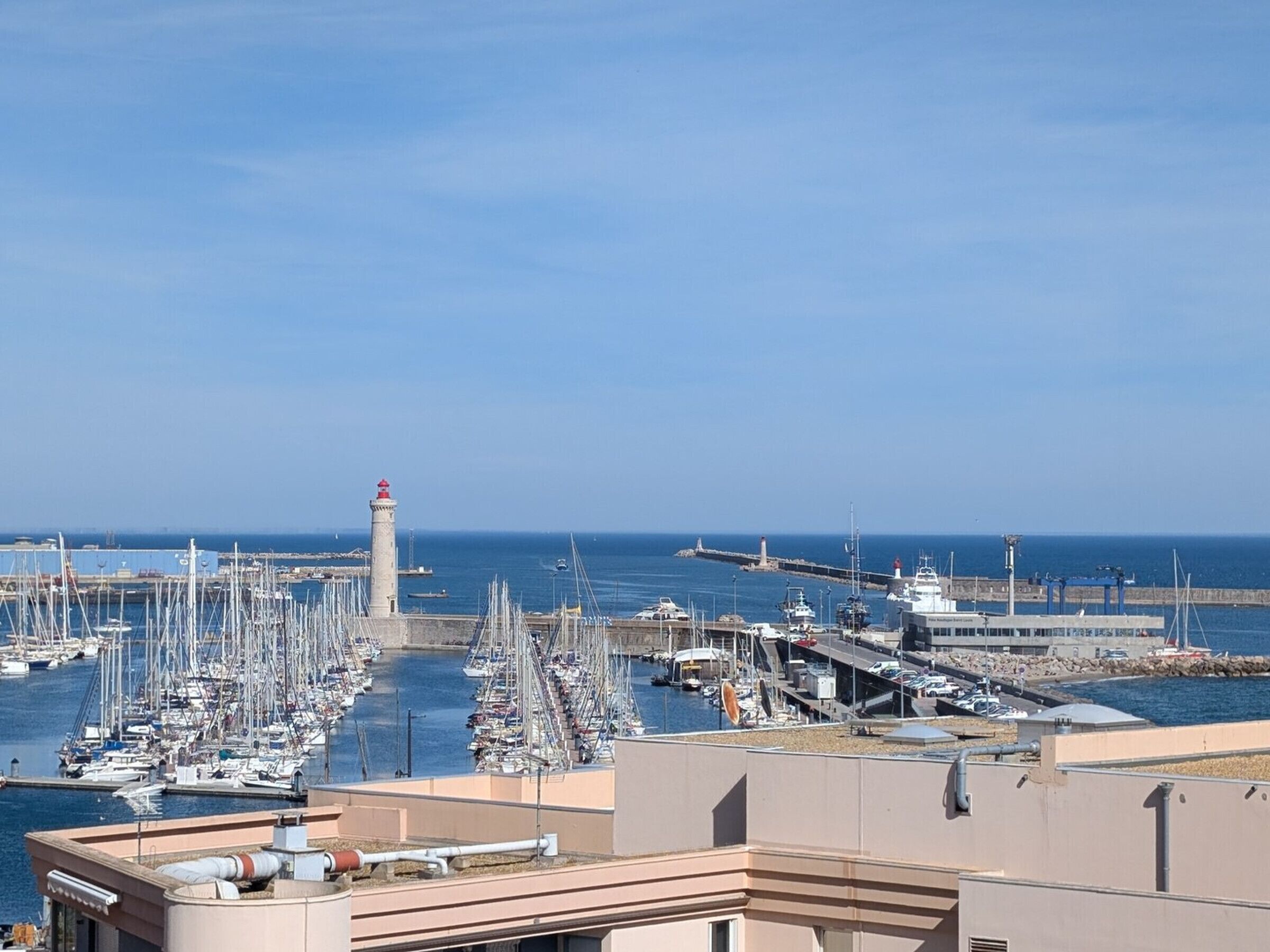 A marina with numerous boats docked, a lighthouse, and a clear blue sky.