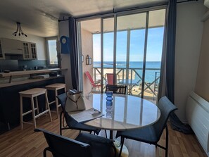 Uma cozinha moderna com vista para o mar, um espaço de jantar com mesa e cadeiras, e uma varanda com uma cadeira.
