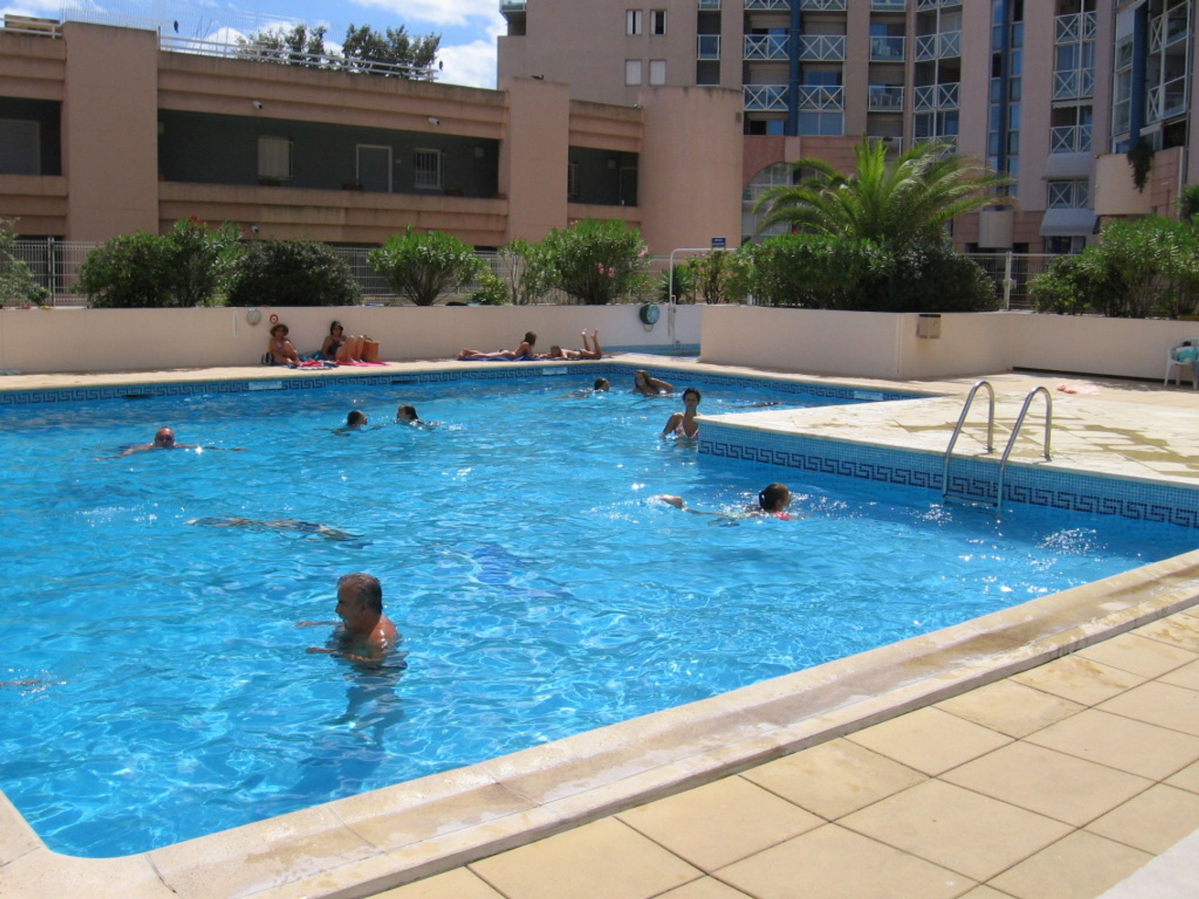 A swimming pool with multiple people swimming and sunbathing.