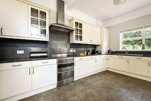 A modern kitchen with white cabinetry, a stainless steel range, and a large window with a view of greenery. - Birchwood House London (Greater London)