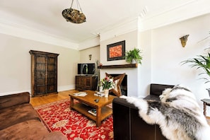 A living room with a brown sofa, a wooden coffee table, a fireplace, and a television. - Birchwood House London (Greater London)