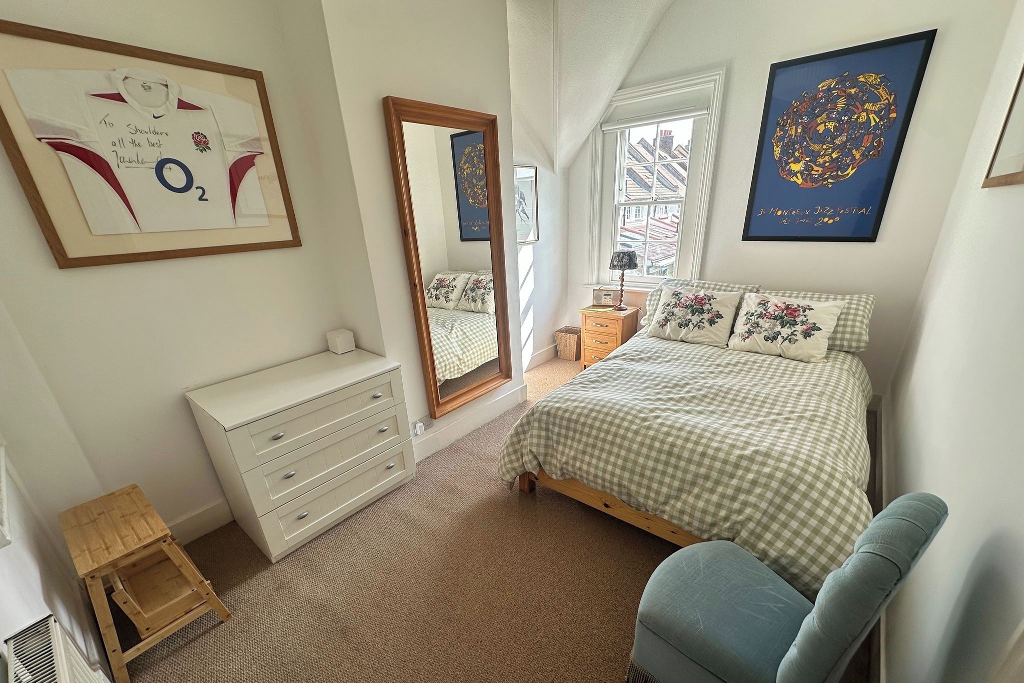 A bedroom with a bed, dresser, chair, and artwork on the walls.