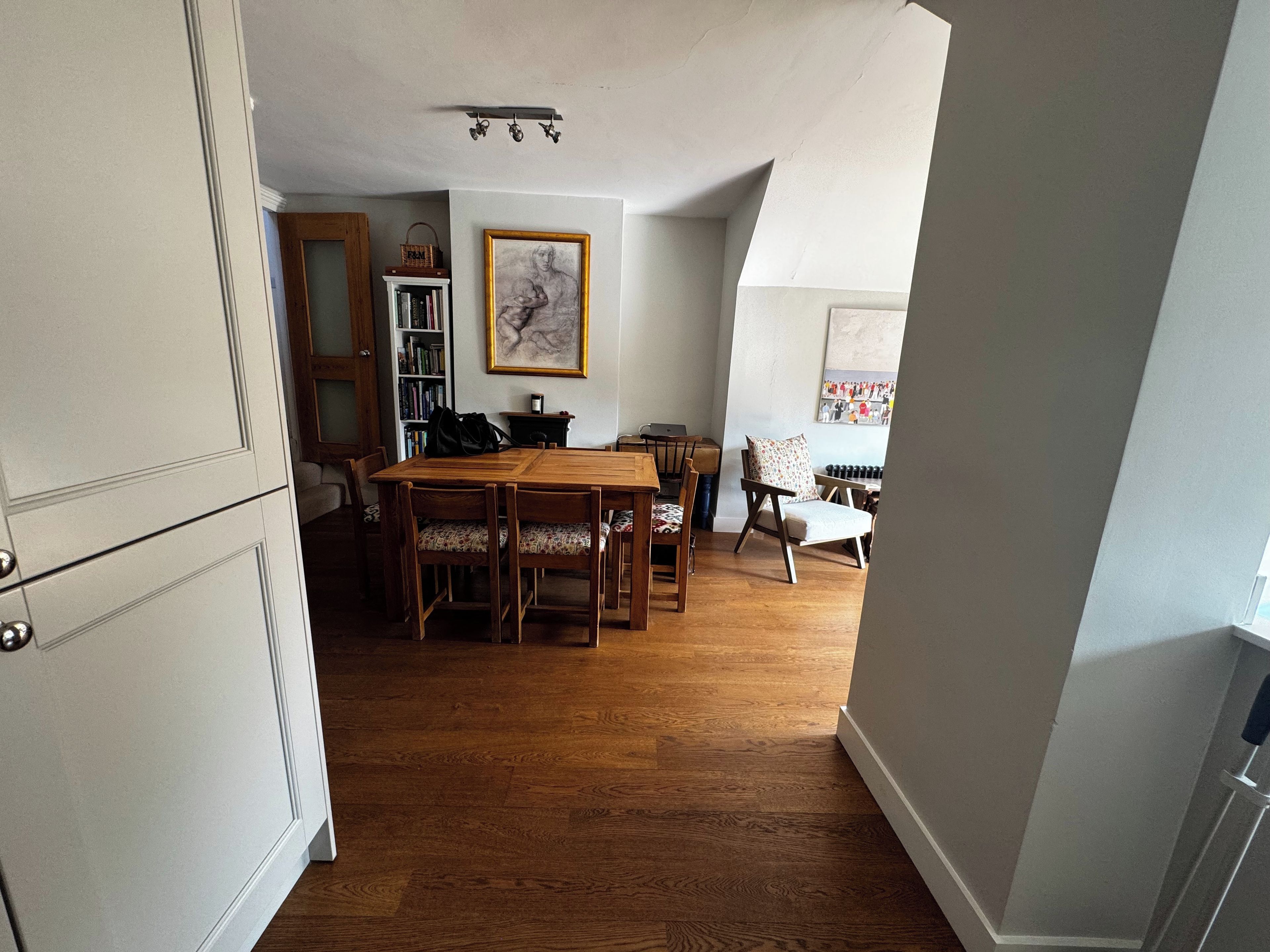 A dining area with a wooden table and chairs, a bookshelf, and a framed artwork on the wall.
