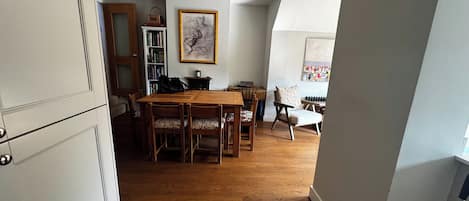 A dining area with a wooden table and chairs, a bookshelf, and a framed artwork on the wall.