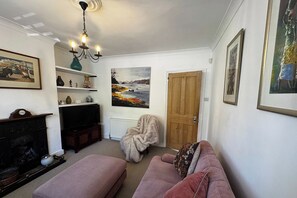 A living room with a fireplace, a television, a sofa, and a door. - Characterful 3BDR Home with Garden in Merton Park (Greater London)