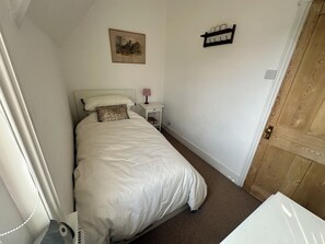 Ein Schlafzimmer mit einem Bett, einem Nachttisch mit Lampe, einem gerahmten Bild an der Wand und einer Holztür.