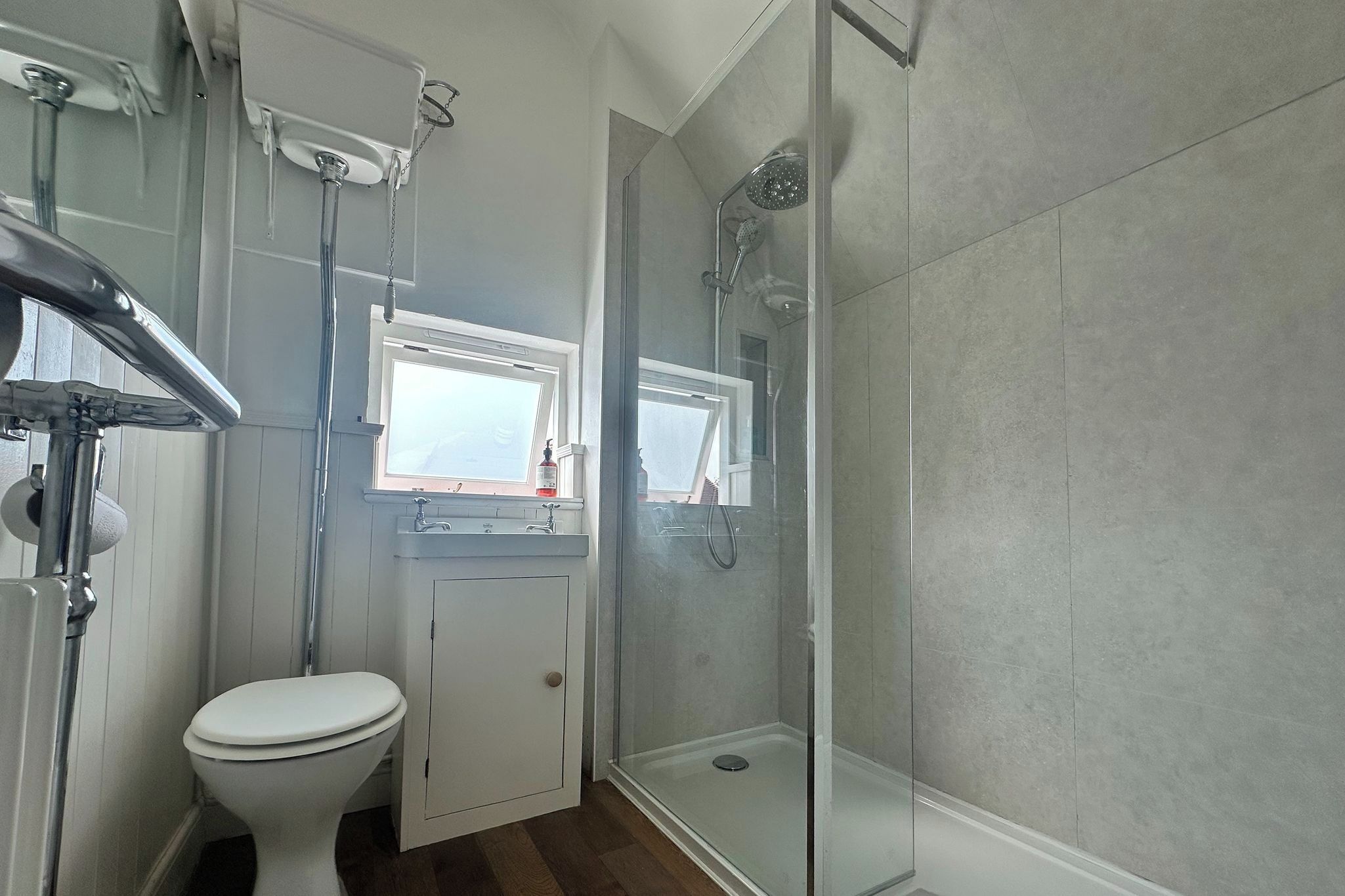 A bathroom with a toilet, a sink, a shower, and a window.