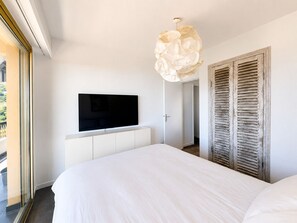 Ein modernes Schlafzimmer mit einem großen Bett, einem Flachbildfernseher an einem weißen Schrank und einer Holztür mit Fensterläden.