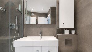 Et moderne badeværelse med en brusekabine i glas, en hvid vask med et spejl over, og et toilet.