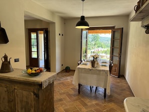 A kitchen with a dining table set for two, a hanging light fixture, and a view through an open door. - Casa Viviani by Interhome (Lucca)