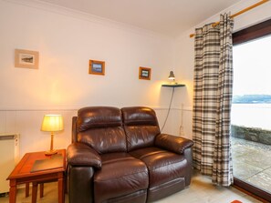 A brown leather sofa in a room with a view of a body of water through a window with plaid curtains. - Aldena 12a South Snowdon Wharf (Porthmadog)