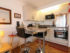 A compact kitchen with a central island, a microwave, a stainless steel refrigerator, and an oven. - Aldena 12a South Snowdon Wharf (Porthmadog)