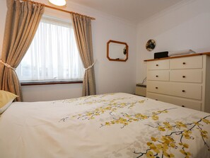 A bedroom with a bed, a dresser, a mirror, and a window with curtains. - Aldena 12a South Snowdon Wharf (Porthmadog)