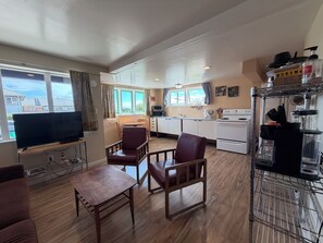 Ein kompakter Wohnbereich mit Fernseher, Sitzecke, Küchenzeile und Blick ins Freie.