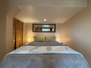 A hotel room with a bed, bedside lamps, a mirror, and a wardrobe.