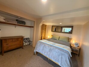 A bedroom with a bed, a dresser, a mirror, and a bedside table with a lamp.