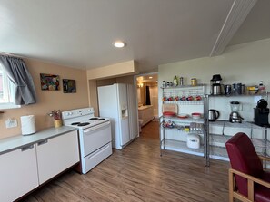 A compact kitchen with white appliances, a wooden floor, and a metal rack with kitchenware.