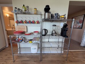 A kitchen with a metal shelving unit holding various kitchenware, a coffee maker, and a blender.