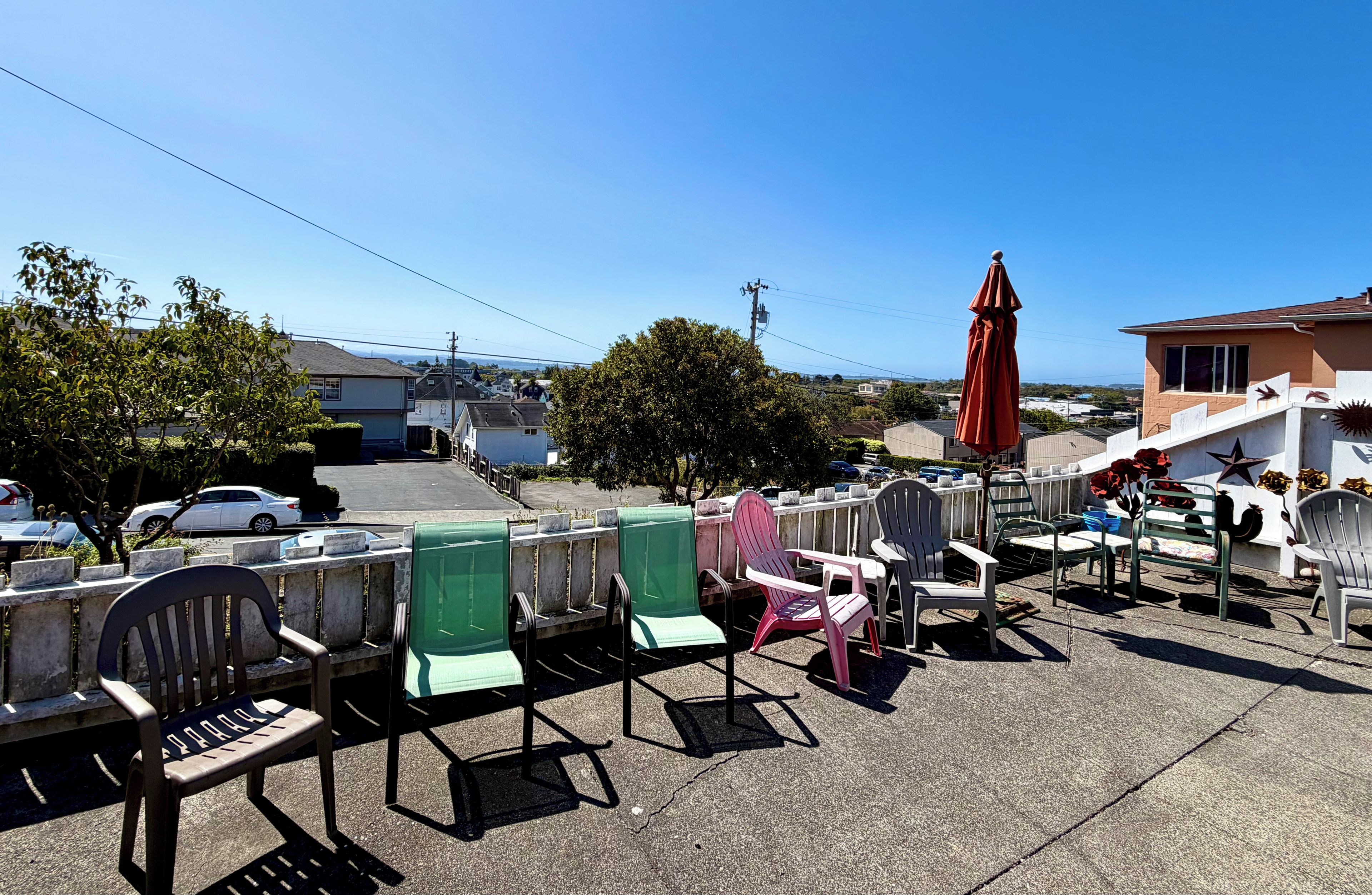 Outdoor seating with chairs and tables, a red umbrella, and a view of a residential street.