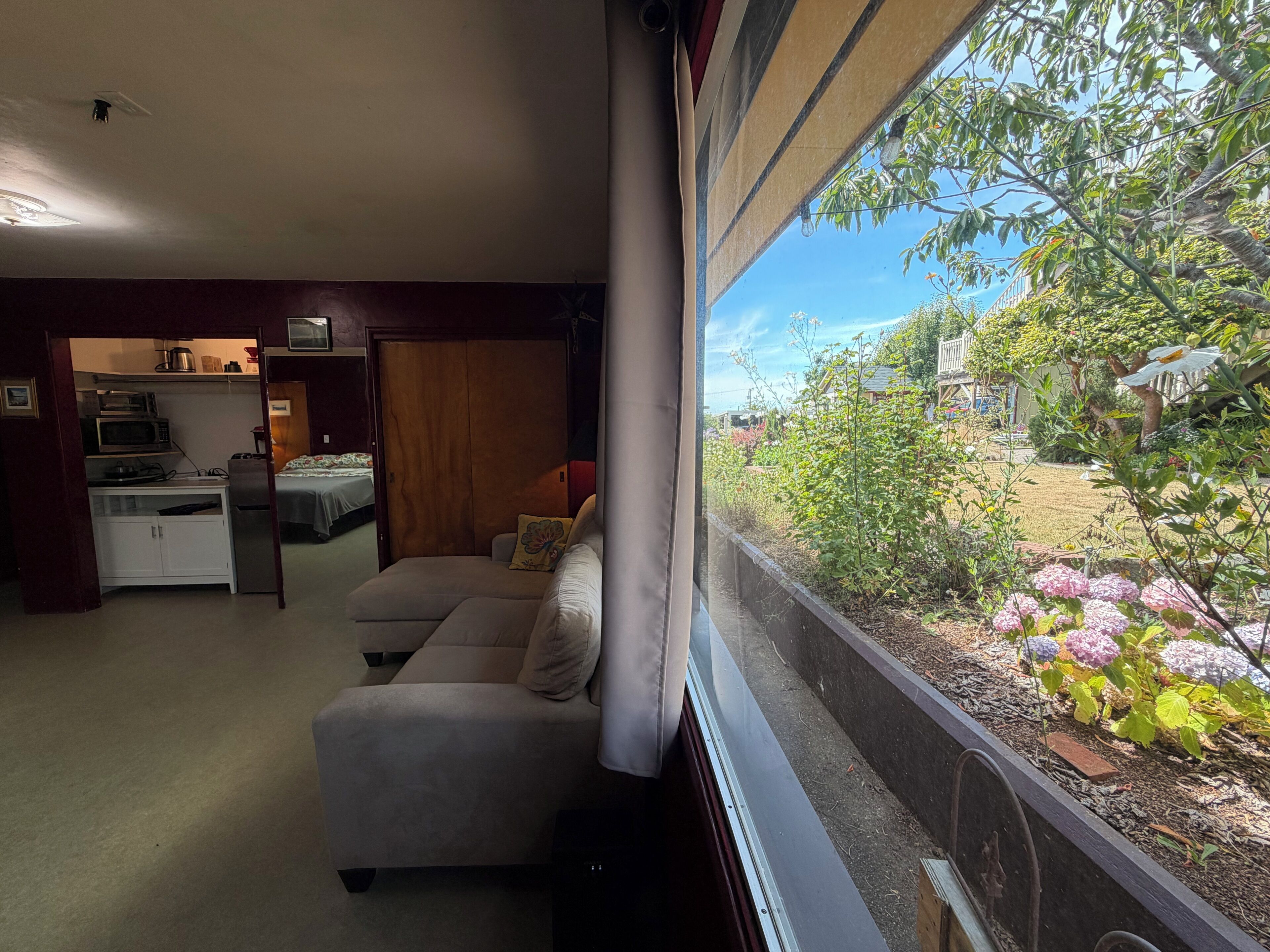 Ein Zimmer mit einer Sitzecke, einer Küchenzeile und Blick auf einen Garten mit Blumen.