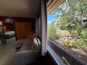 A room with a sofa, a bed, and a window overlooking a garden.