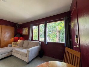 A room with a beige sofa, a wooden table, a red wall, and a window with curtains.