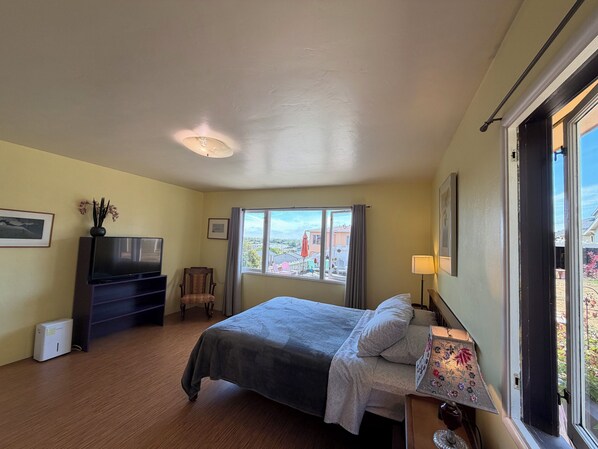 A hotel room with a bed, a television, a chair, a window with a view, and a lamp.